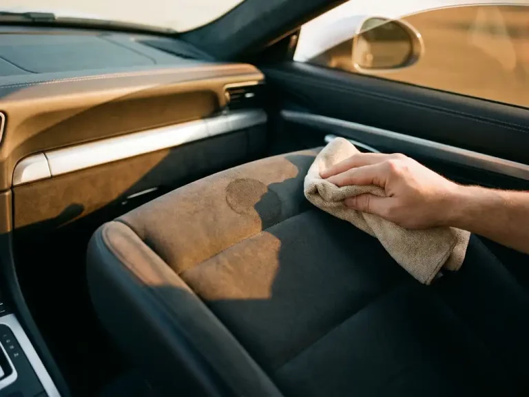 Microvezel doek behandelt donkere vlek op grijze alcantara autostoel, luxe leren dashboard op achtergrond