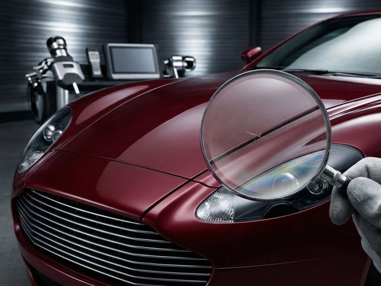 Vergrootglas inspecteert verfschade en paneelkieren op rode supercar tijdens professionele autokeuring