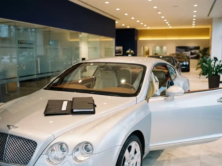 Zilveren Bentley Continental GT in luxe showroom met financieringscontract op motorkap en crème lederen interieur zichtbaar