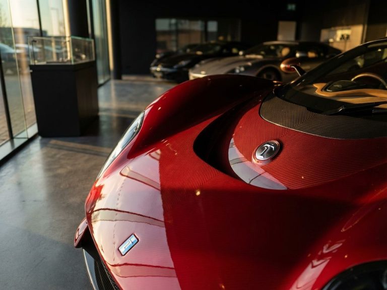 De Tomaso P72 supercar close-up toont koolstofvezel carrosserie en aerodynamische lijnen in gouden showroomlicht