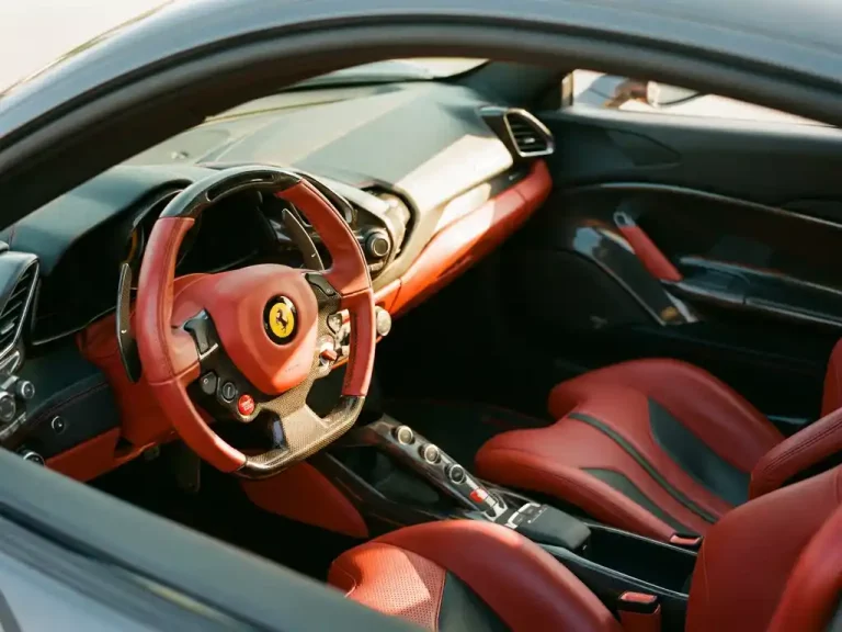 Ferrari interieur met handgestikt rood leer, carbon fiber dashboard en stuurwiel in gouden zonlicht