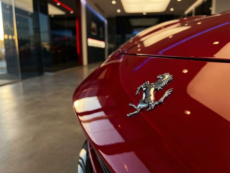 Ferrari prancing horse embleem op rode motorkap in luxe showroom met gouden verlichting en donkere achtergrond