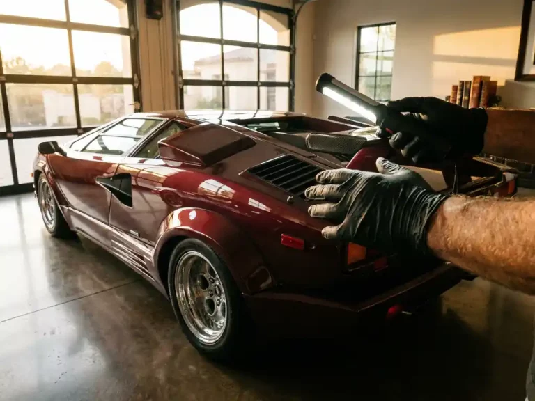 Vintage Lamborghini Countach wordt door expert met handschoenen geïnspecteerd in luxe garage met gouden zonlicht