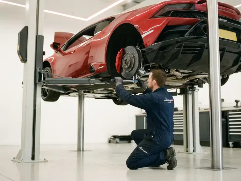 Rode Lamborghini sportwagen op hydraulische lift terwijl monteur remsysteem inspecteert in witte garage