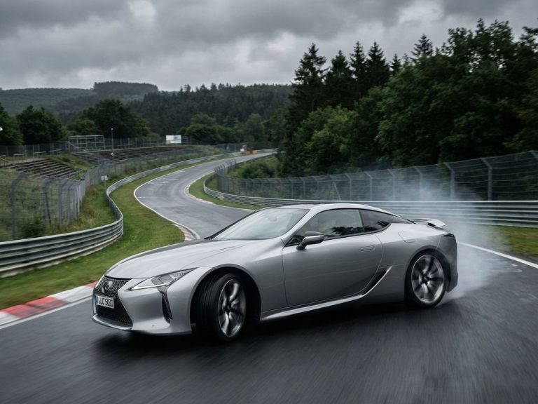 Zilveren Lexus sportwagen neemt bocht op Nürburgring circuit met bewegingsonscherpte en bandenrook