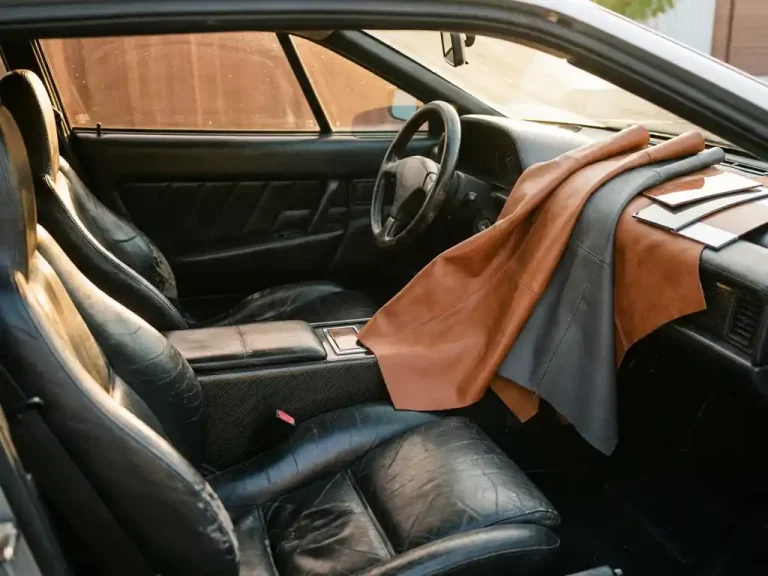 Versleten zwarte leren autostoelen naast nieuwe cognac en antraciet leermonsters op dashboard, gouden zonlicht benadrukt textuurcontrast