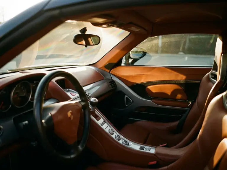 Luxe sportwagen interieur met cognac leren stoelen en dashboard in gouden zonlicht, UV-beschermingsfolie zichtbaar op voorruit