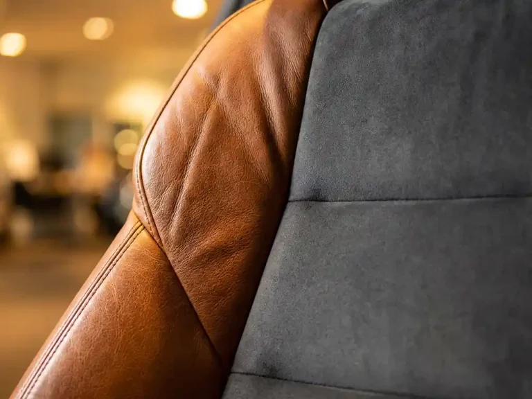 Luxe autostoel met cognac leer en grijze alcantara bekleding in warme showroomverlichting