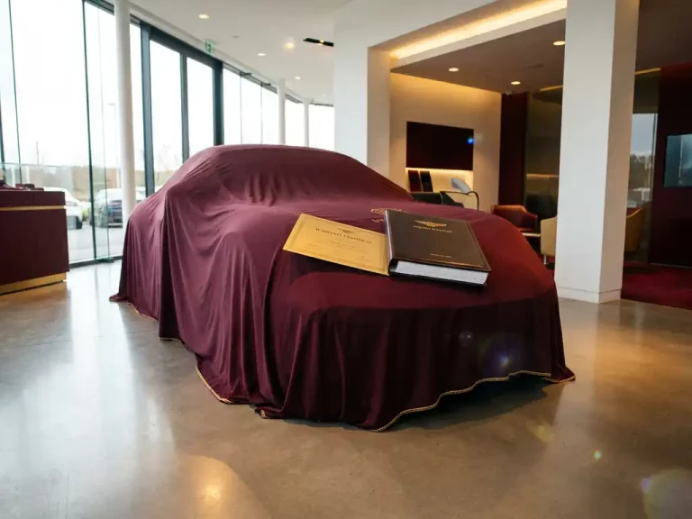 Luxe sportwagen onder elegante beschermhoes in moderne showroom met garantiecertificaat en serviceboekje op motorkap
