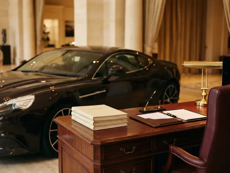 Zwarte luxe sportwagen naast mahonieholten bureau met financiële documenten en gouden vulpen in warm verlichte showroom