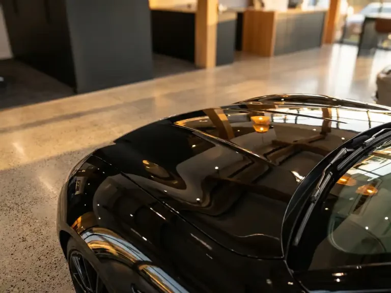 Glanzende zwarte motorkap van luxe sportwagen met keramische coating reflecteert gouden zonlicht in chique showroom