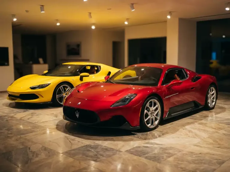 Rode Maserati sportwagen voor gele Ferrari in luxe autoshowroom met marmeren vloer en dramatische verlichting