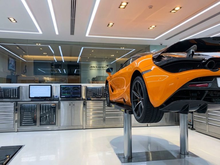 Oranje McLaren sportwagen op hydraulische lift in moderne garage met LED-verlichting en professionele gereedschappen