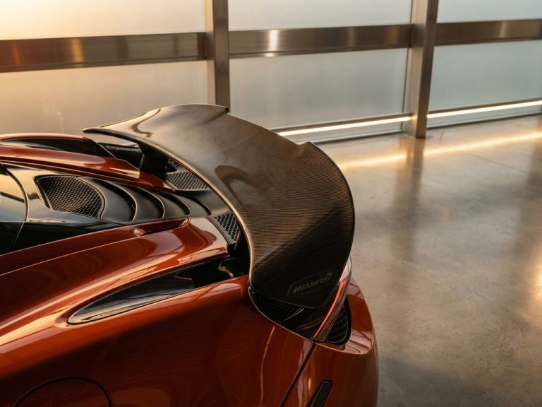 McLaren supercar achtervleugel met oranje en carbon fiber details in moderne showroom met gouden verlichting