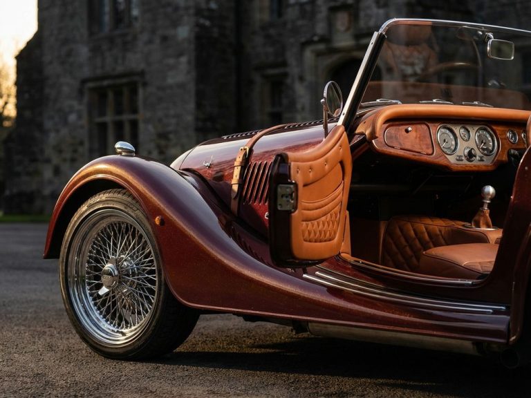 Close-up van klassieke Morgan sportwagen met draadspaakwiel, chromen accenten en bordeauxrode lak in gouden licht
